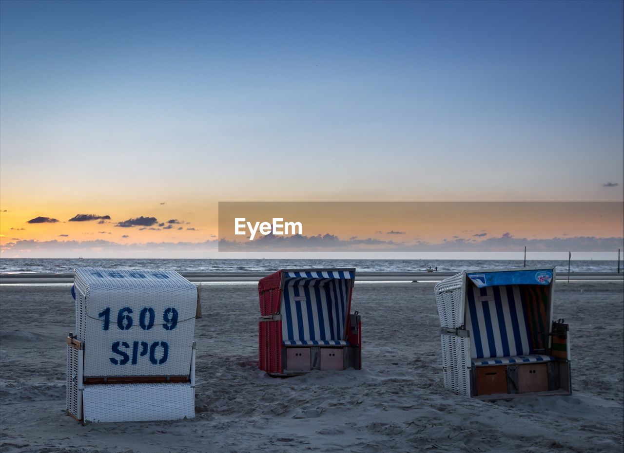 Hooded beach chairs on shore against sky