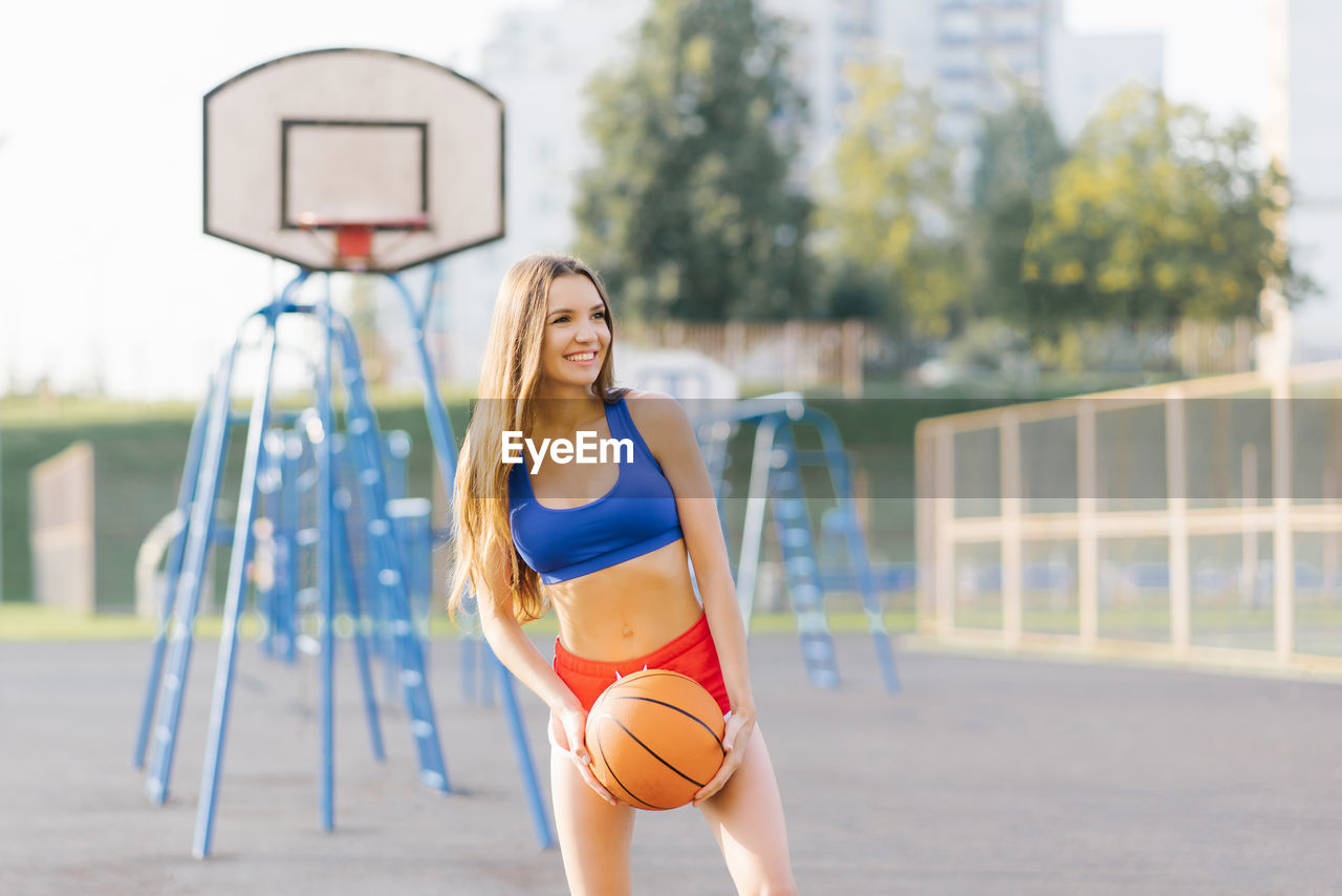 An athletic young woman in sports shorts and t-shirts plays on a basketball court with a ball