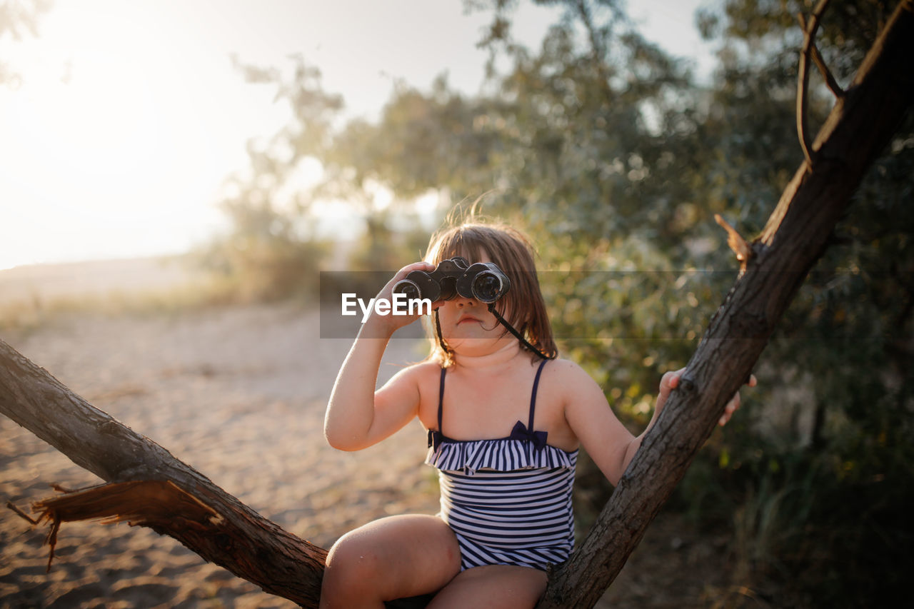 Cute european child girl in bathing suit with binoculars on tree. summer holidays and adventures.