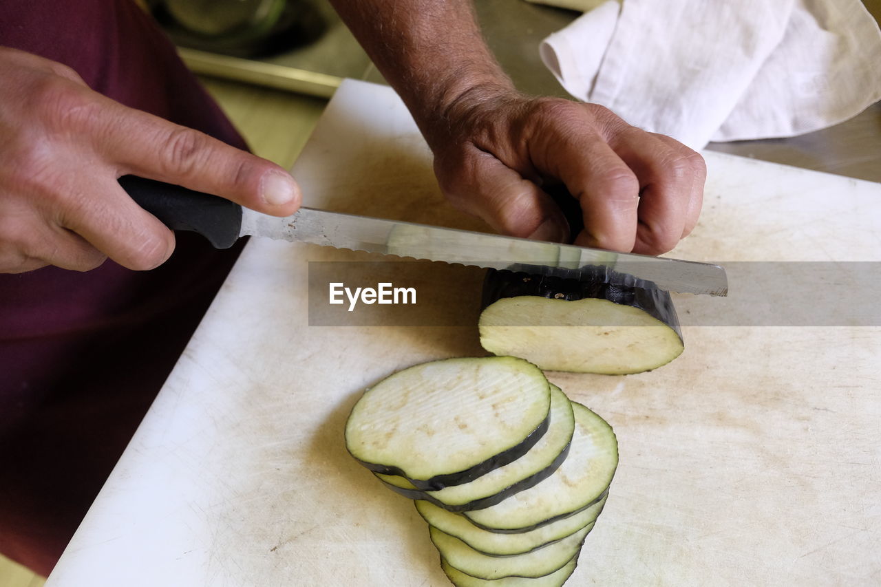 Midsection of man slicing eggplant on kitchen counter