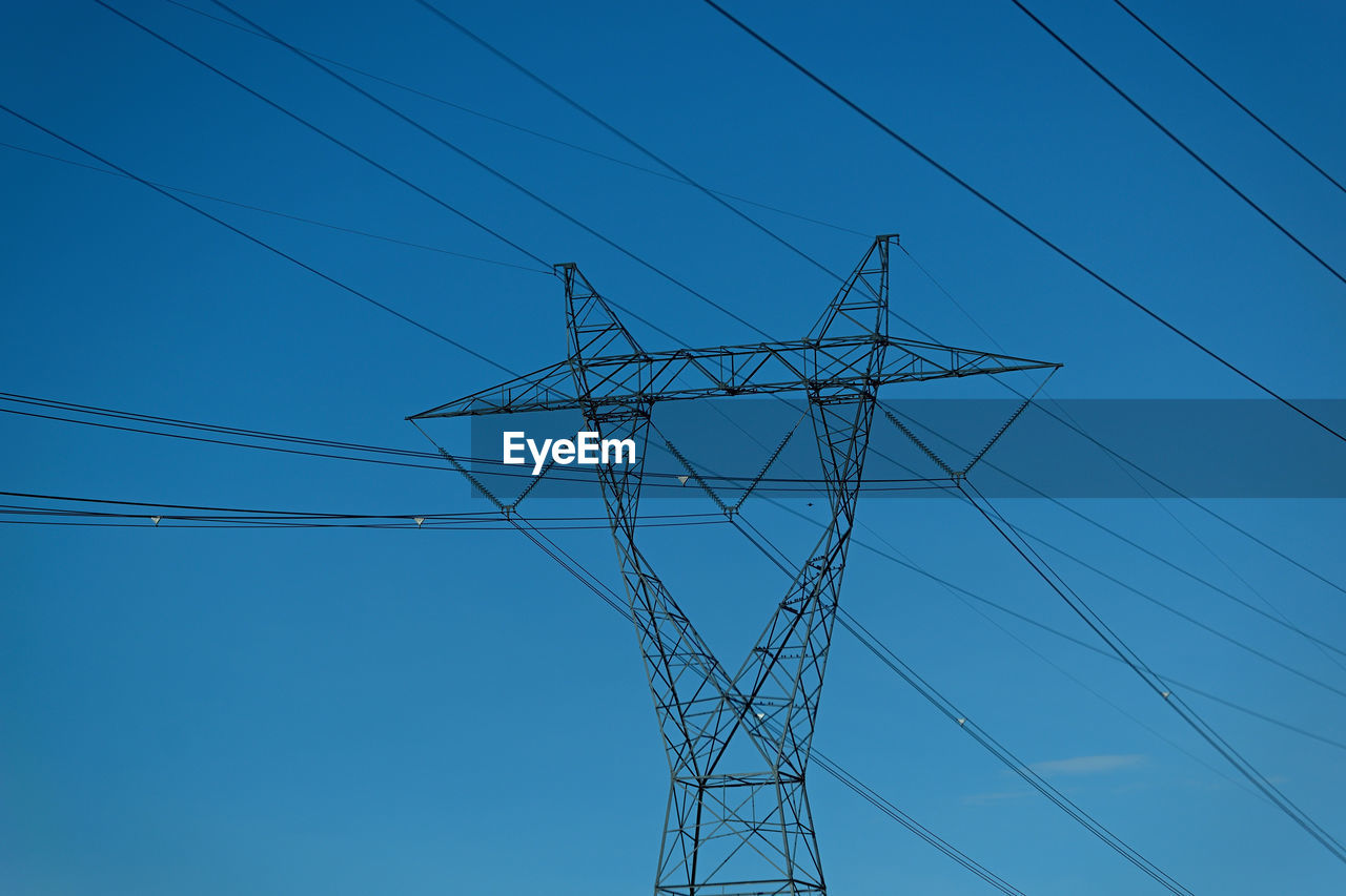 Low angle view of electricity pylon against clear blue sky