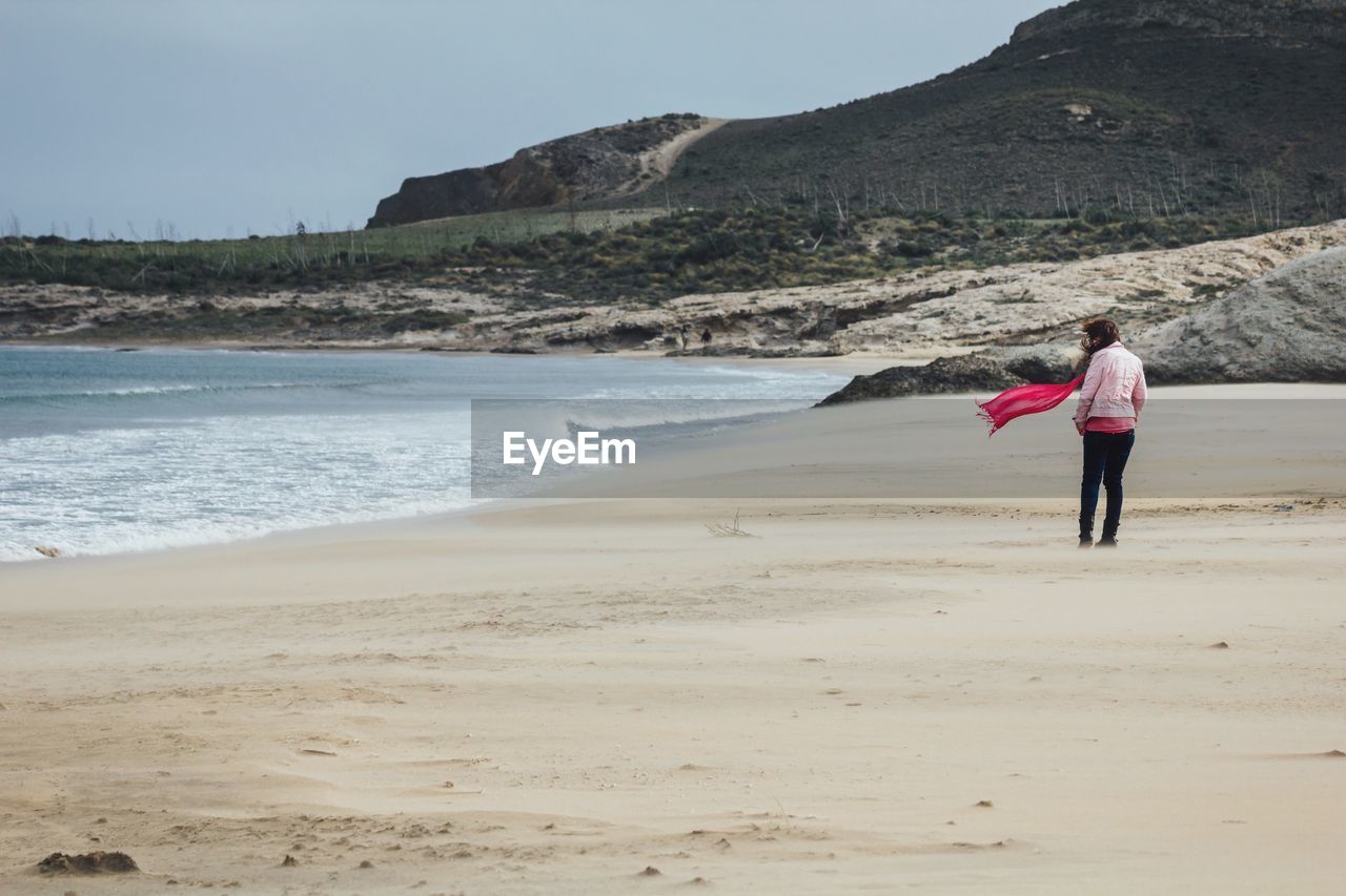 Rear view of woman standing on beach against sky