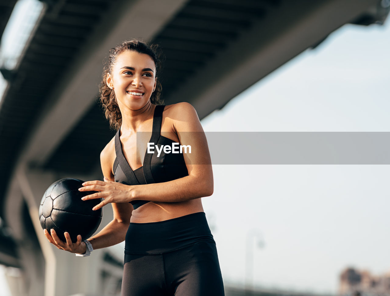 Low angle view of woman exercising with ball standing outdoors