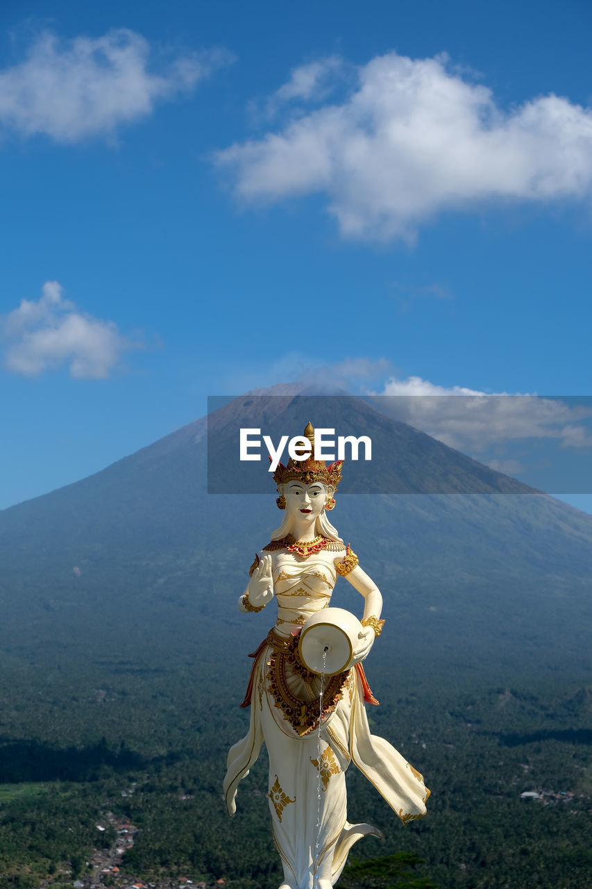 Statue against blue sky and volcano