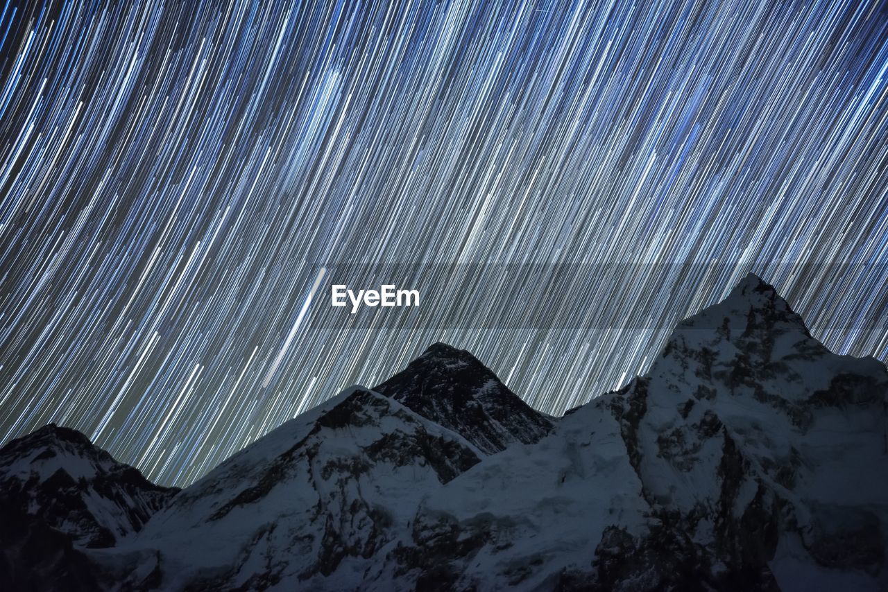 Low angle view of snow covered mountains against star trails