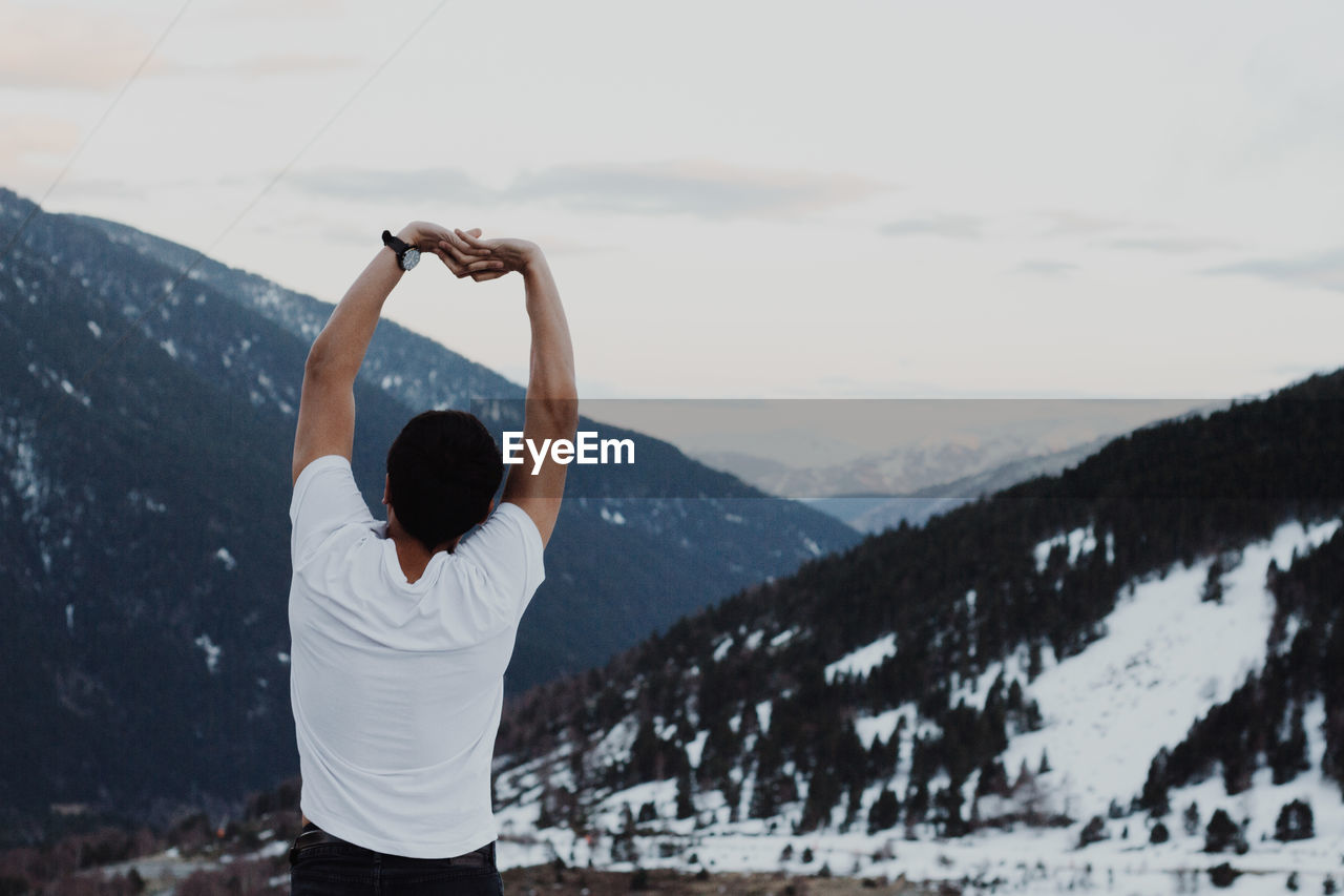 Rear view of man stretching arms against snowcapped mountain