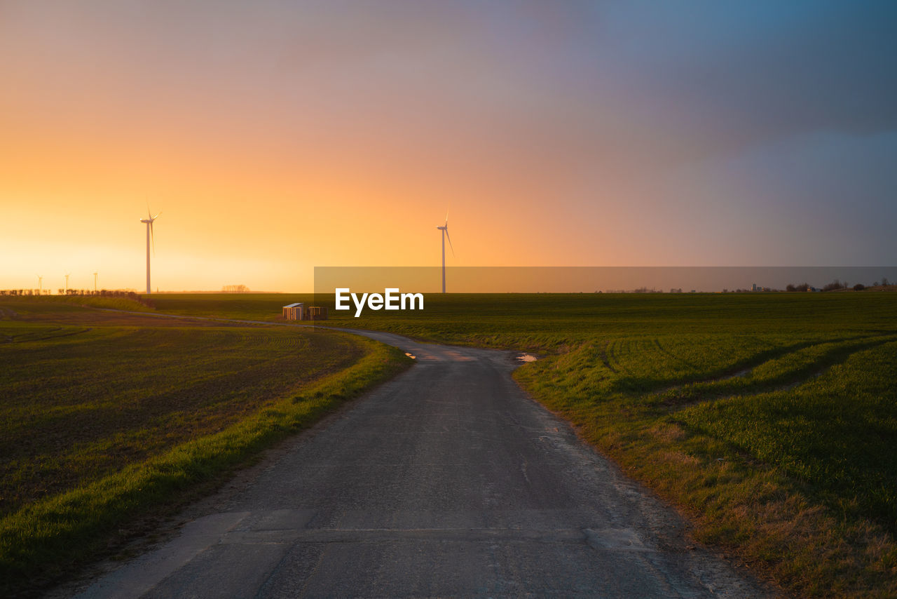 Road amidst field against sky during sunset