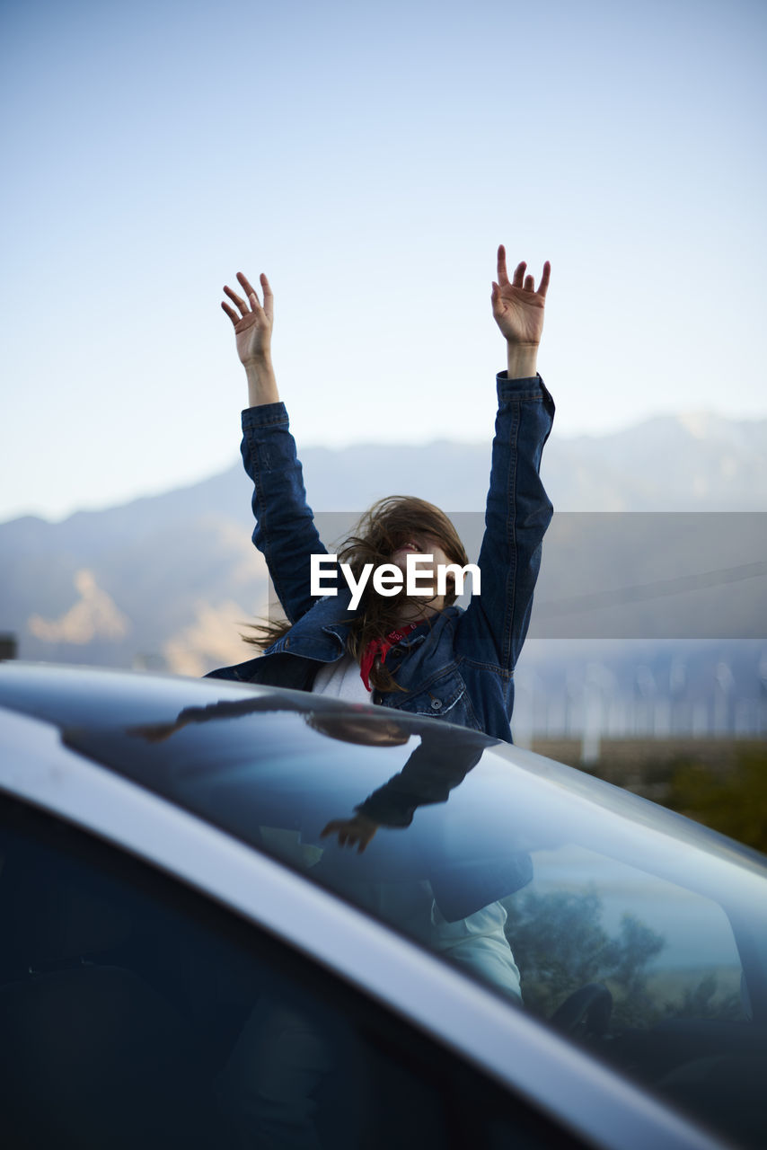 Young woman with arms raised and tousled hair sitting in car