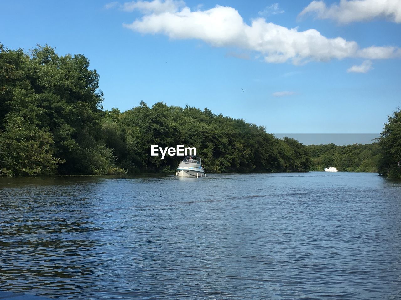 BOAT SAILING ON LAKE BY TREES AGAINST SKY