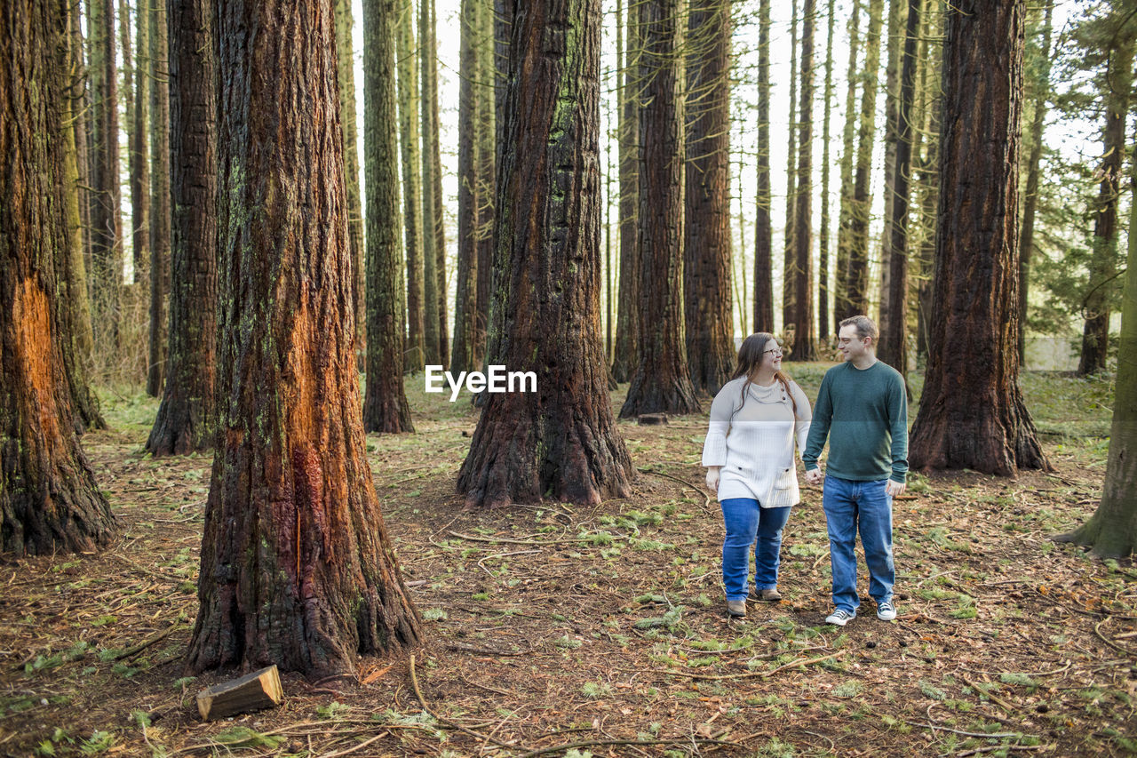 Couple walking through forest, holding hands.