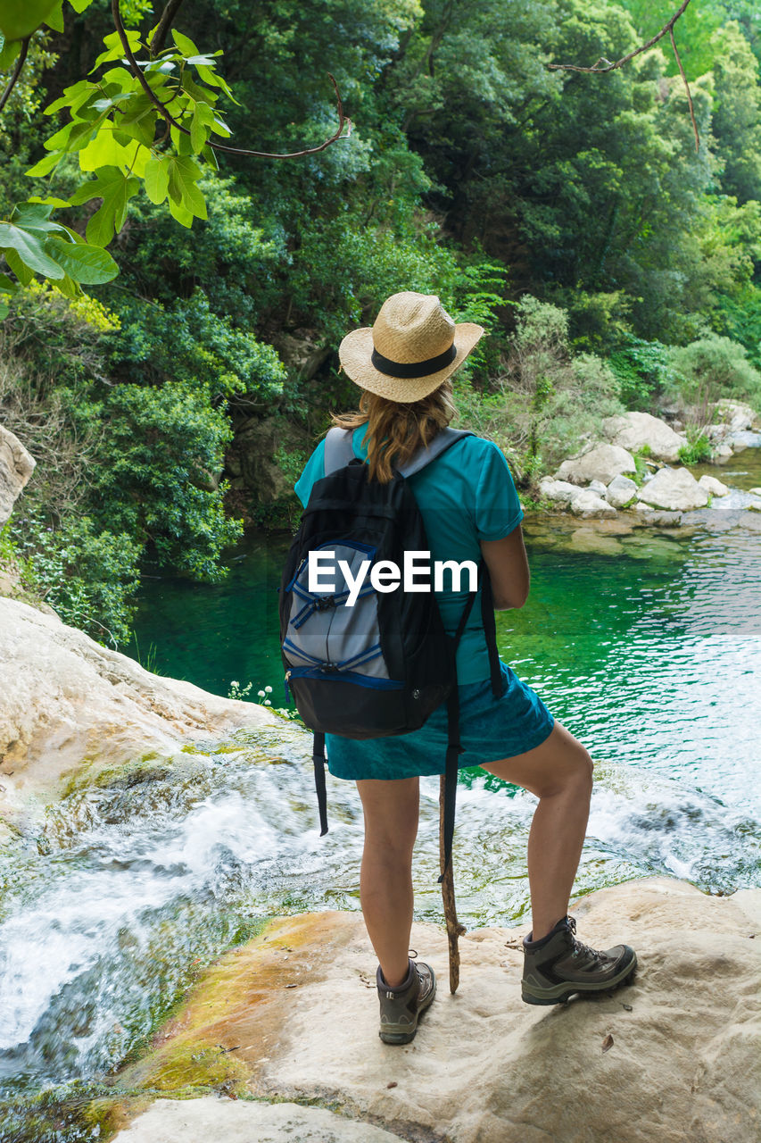 Rear view of woman standing on rock by river