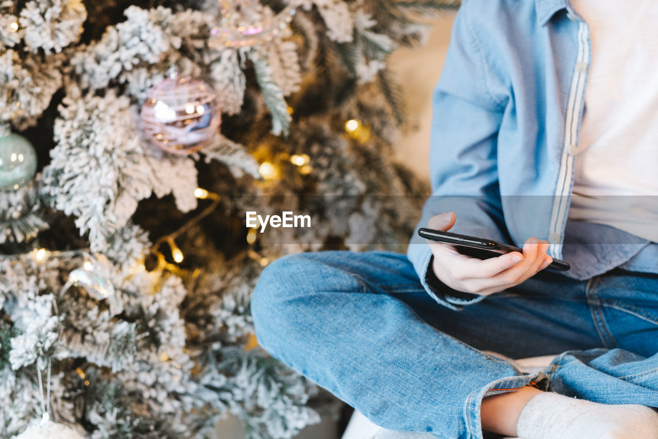 Child with a phone in his hands against the background of a christmas tree, close-up