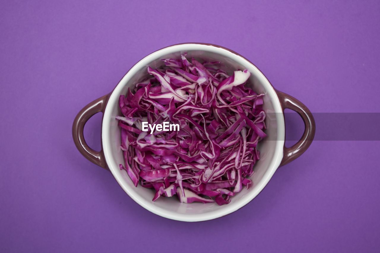 Directly above shot of sliced cabbage in bowl against purple background