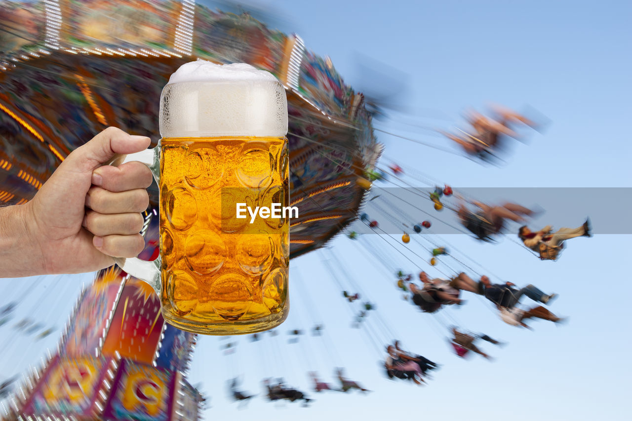 CLOSE-UP OF HAND HOLDING BEER GLASS AGAINST CLEAR SKY