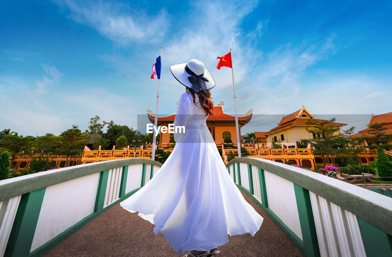 Side view of woman standing on footbridge against sky