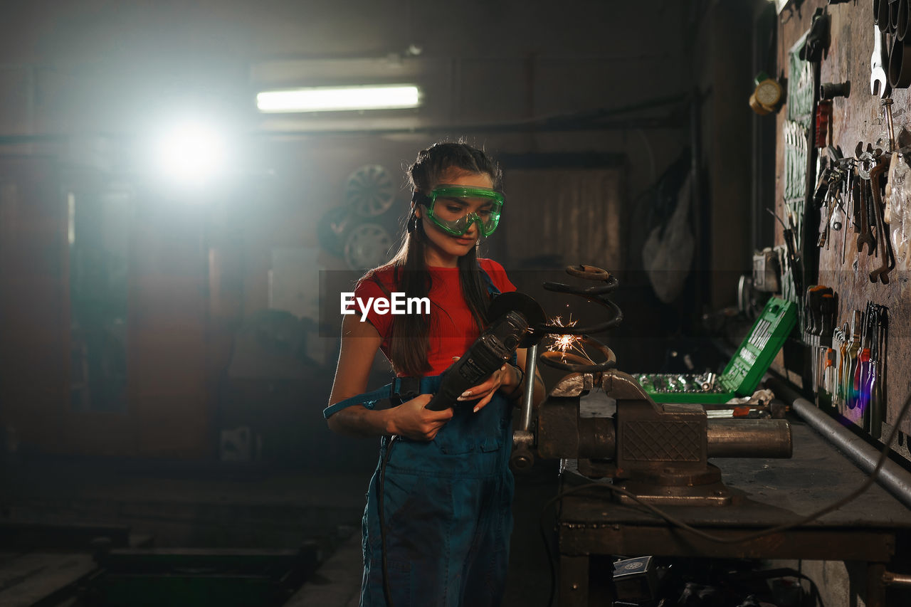 Young woman using grinder while wearing protective glasses at factory