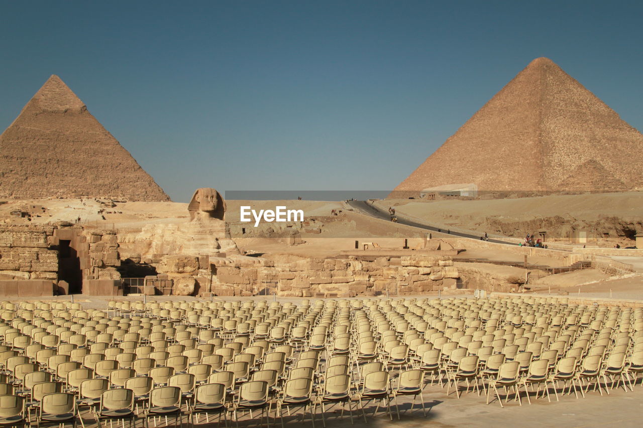 Empty chairs by sphinx and pyramid of khafre against clear sky