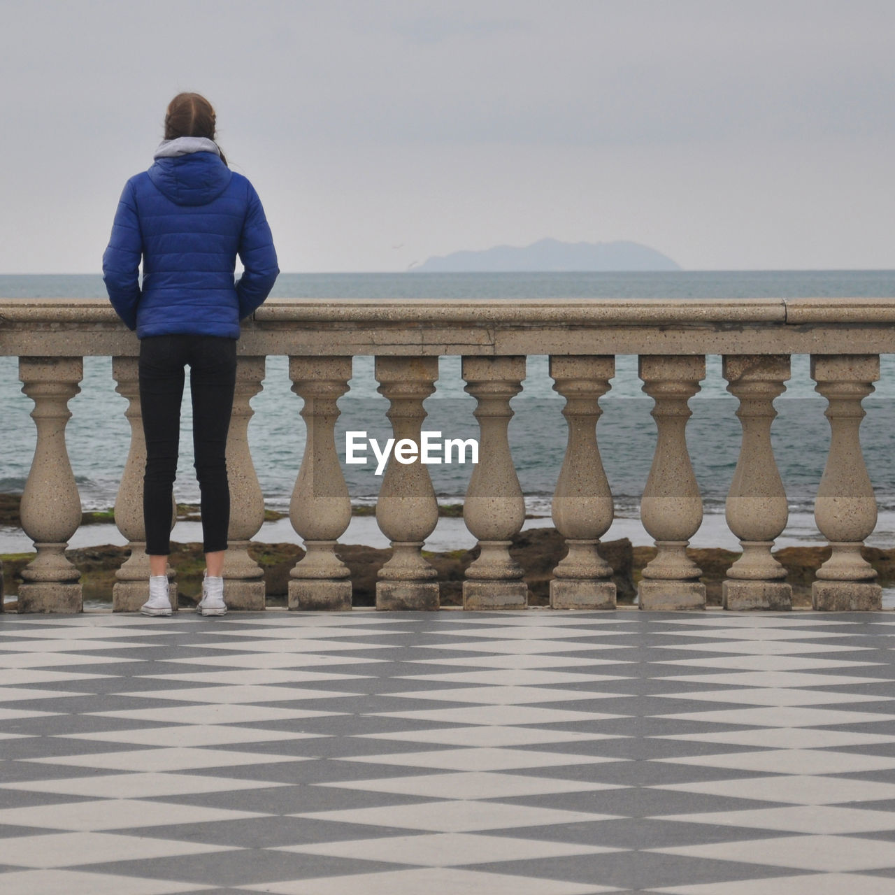 Rear view of woman standing by railing against sea