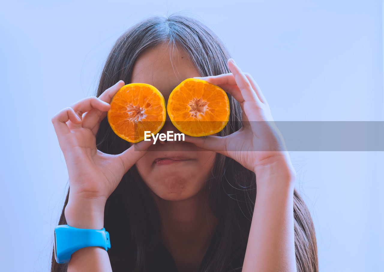 Close-up of girl holding orange slices against clear sky