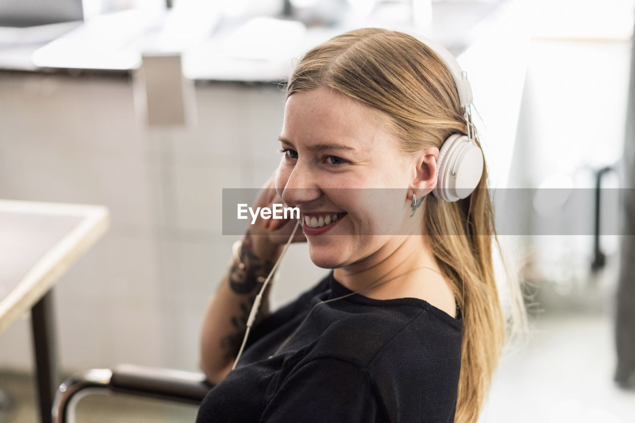 Smiling young businesswoman wearing headphones in creative office