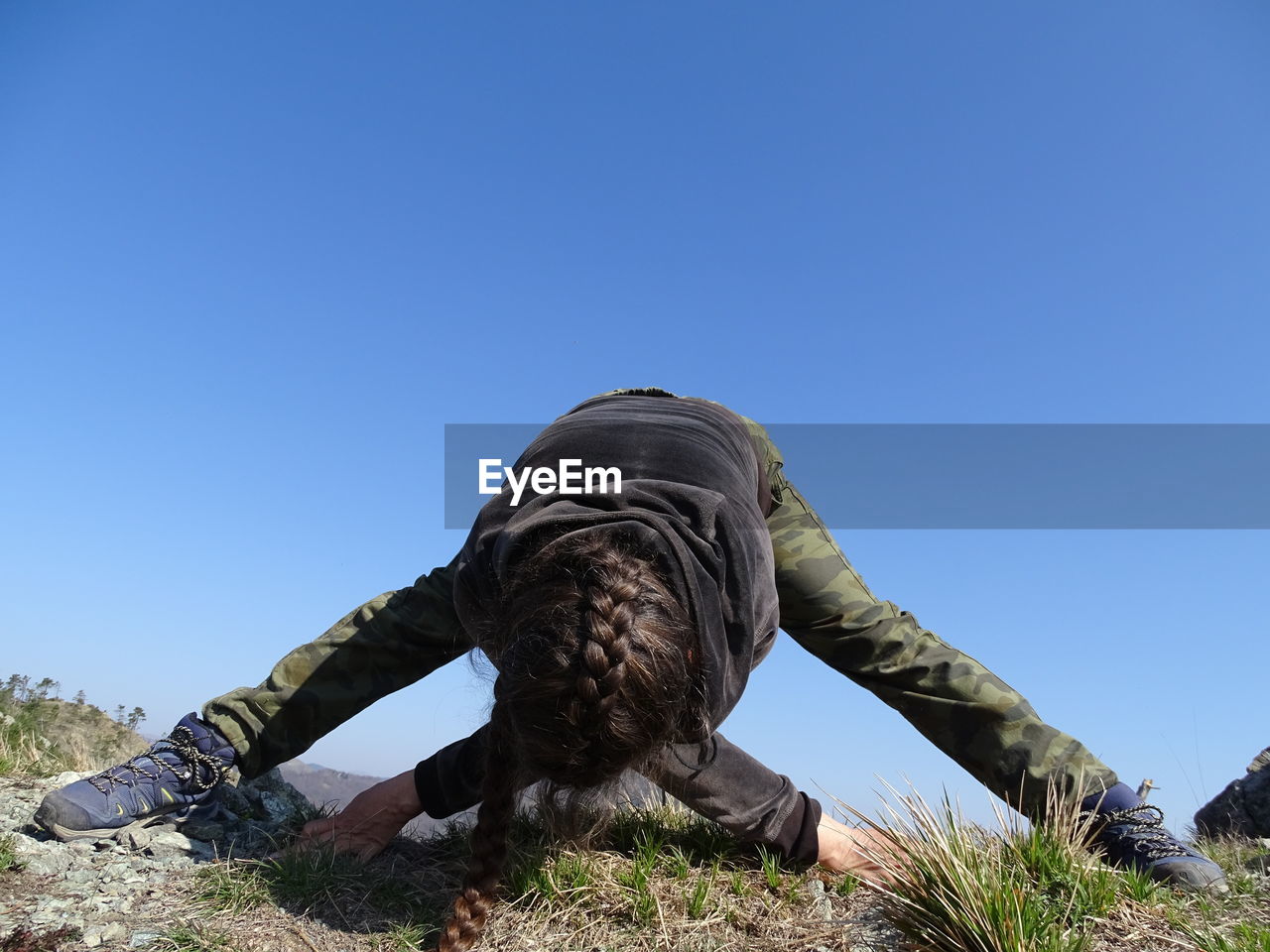 Woman stretching on mountain against clear sky