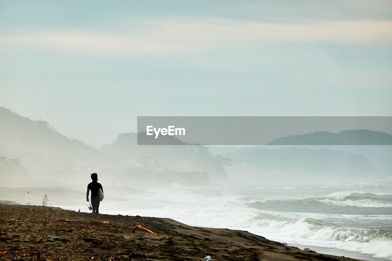 Rear view of man standing on shore against sky