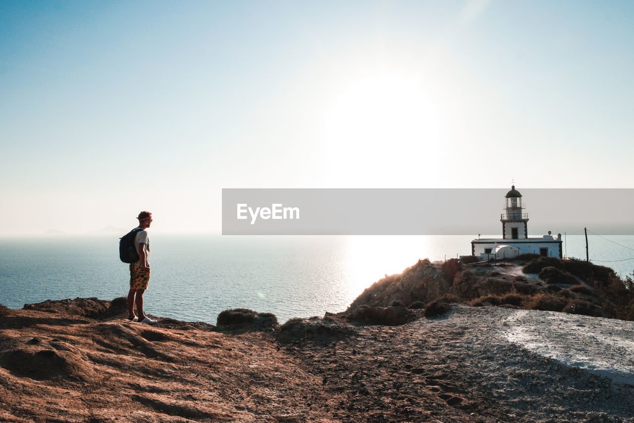 Man standing near lighthouse on cliff by sea against clear sky