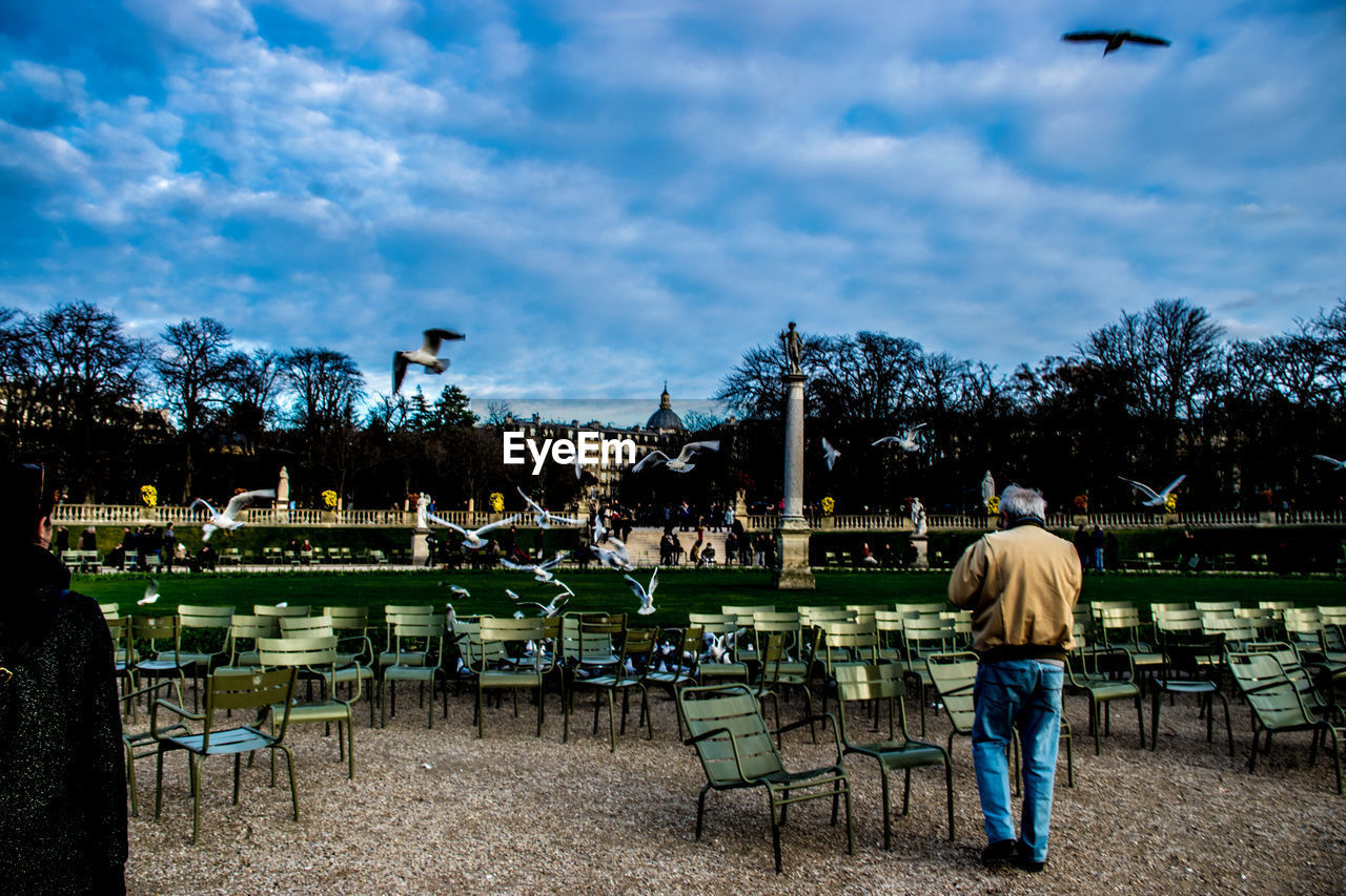 PEOPLE STANDING BY RIVER AGAINST CLOUDY SKY AT DUSK