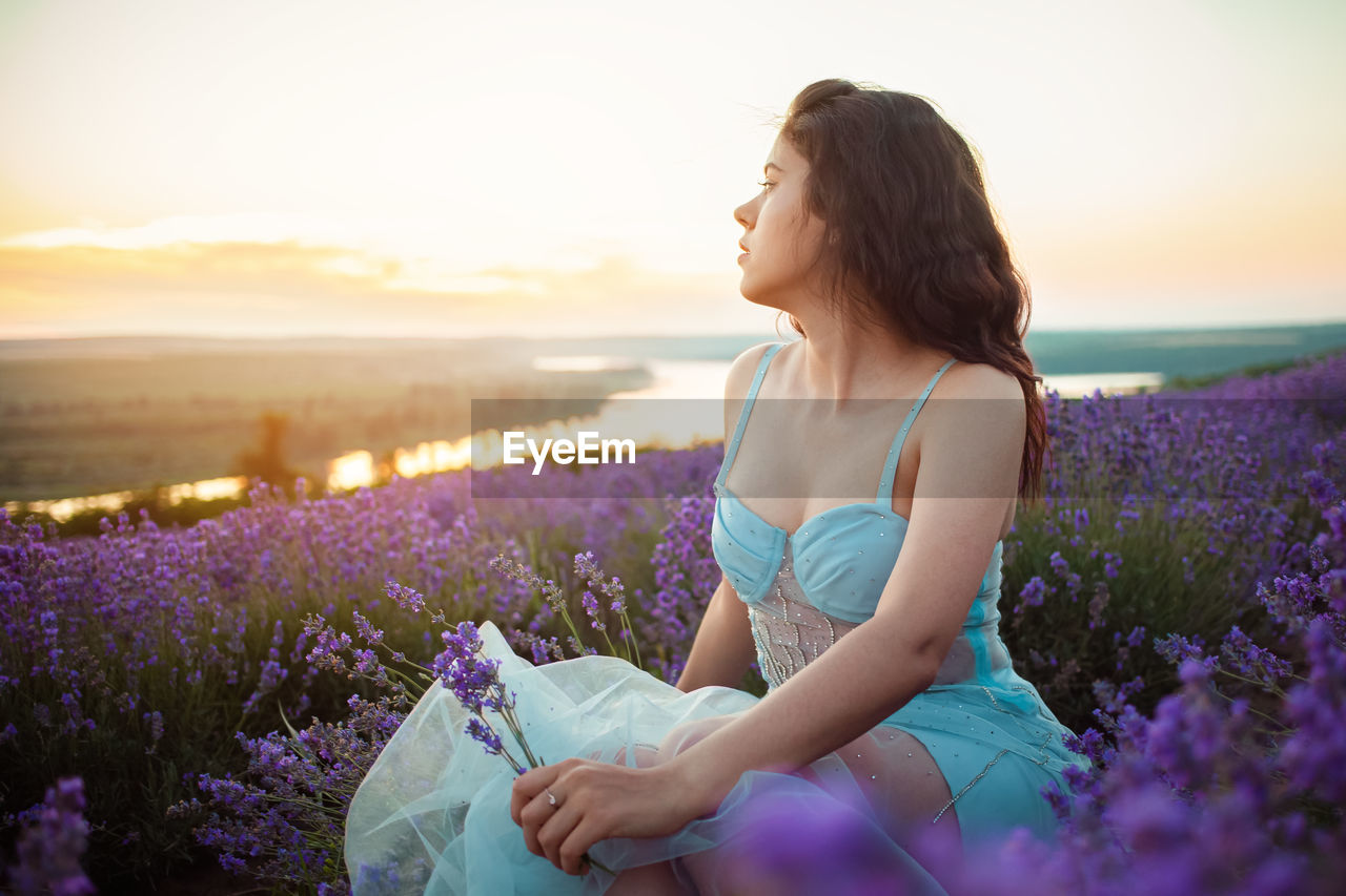 A beautiful young girl against the sunset and a beautiful sky in a lavender field. 