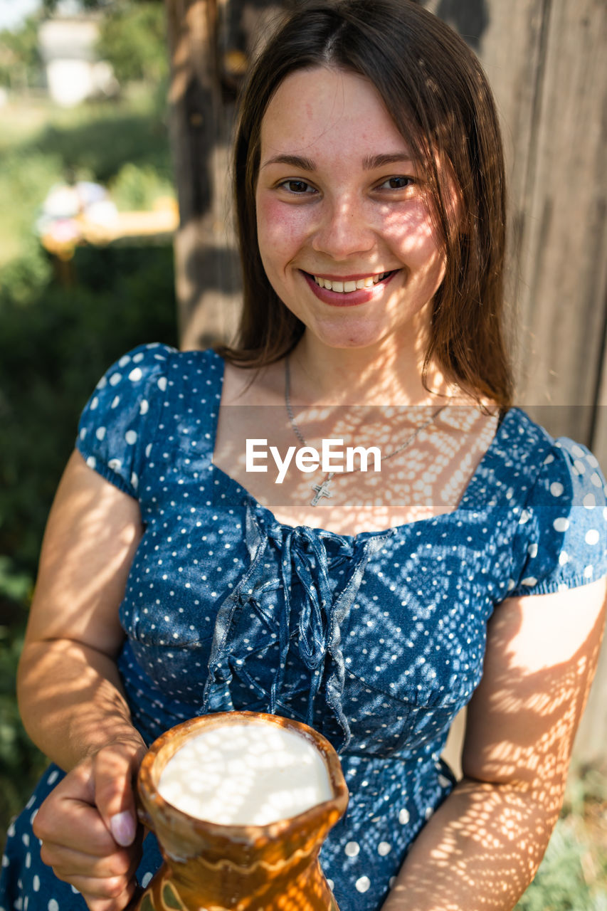 Young cute ukrainian girl holding jug of milk in countryside