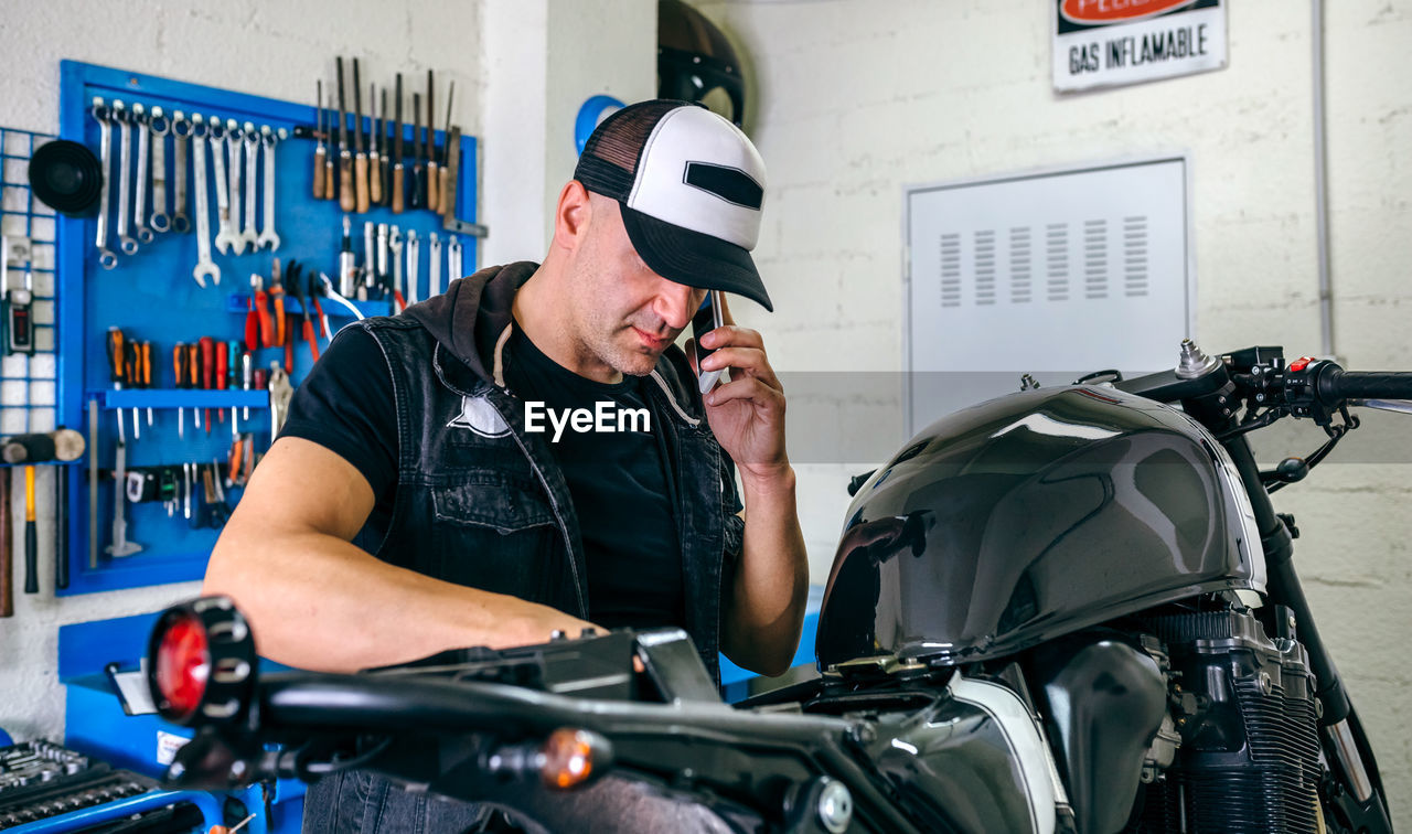 Mature mechanic using phone by motorcycle in garage