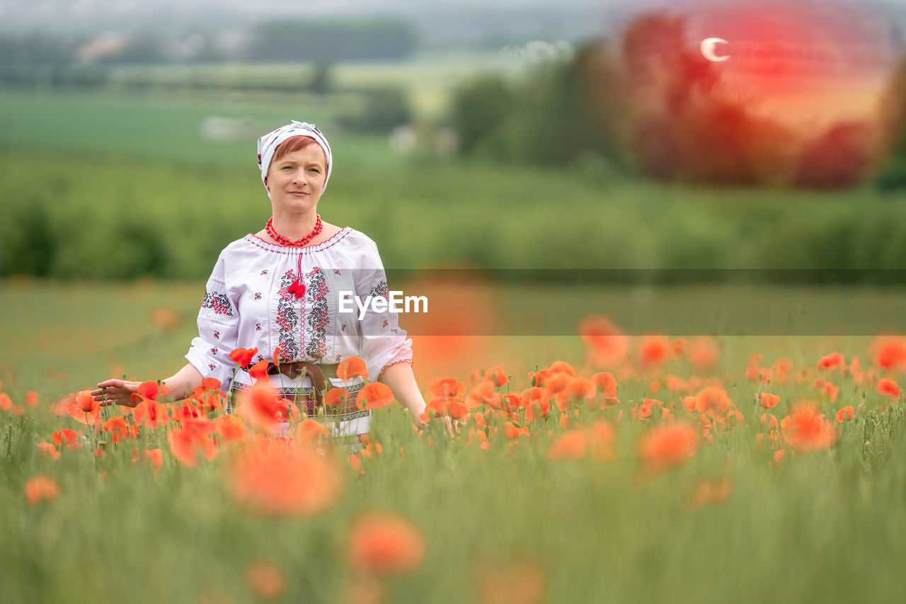 portrait of smiling young woman standing amidst yellow flowering plants on field