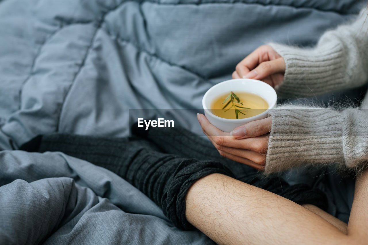 midsection of woman holding coffee cup on bed