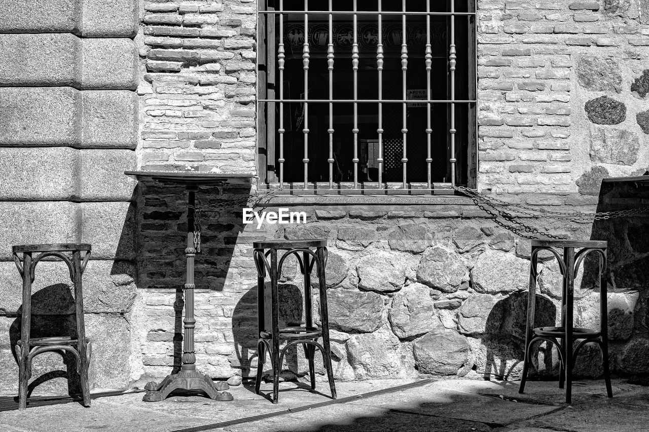 black and white, architecture, built structure, building exterior, monochrome, street, monochrome photography, white, seat, chair, road, black, wall, day, no people, window, building, wall - building feature, house, sunlight, brick, urban area, brick wall, outdoors, closed, iron, history, old, ancient history, footpath