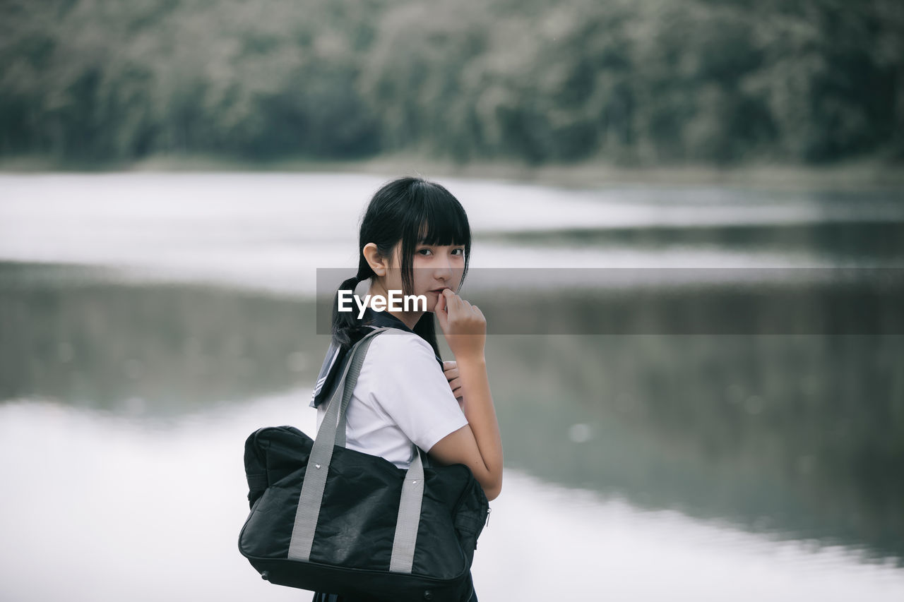 Portrait of young woman standing by lake