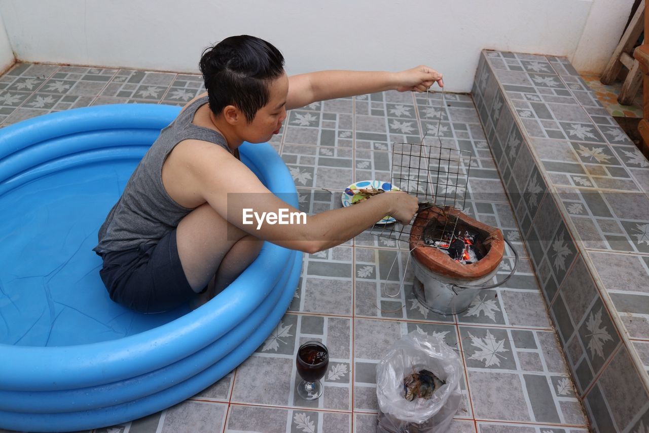 High angle view of woman preparing food on stove while sitting in inflatable pool