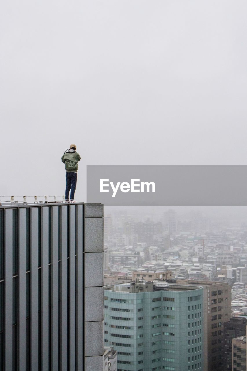 Rear view of man standing on building terrace against sky in city