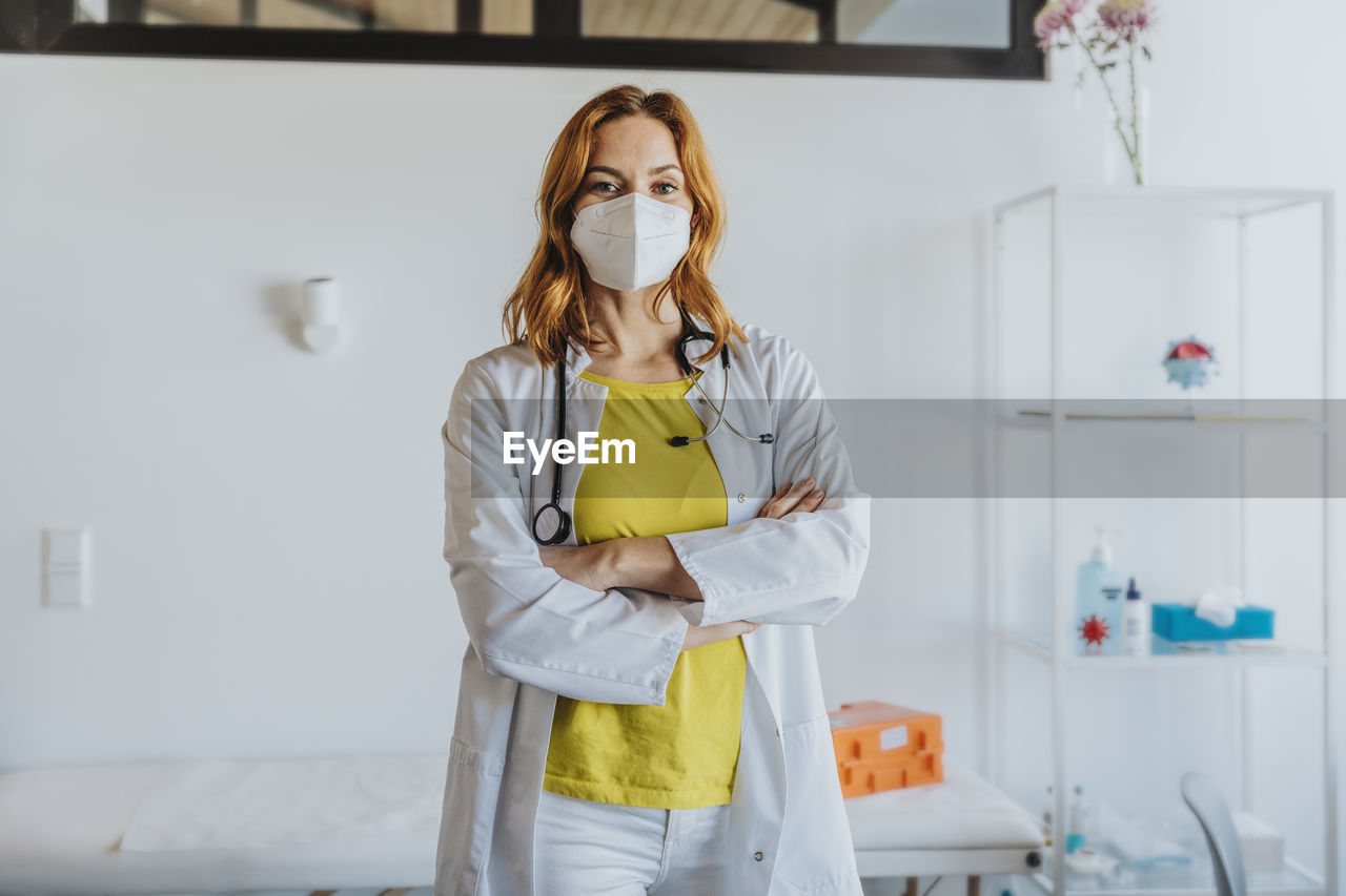 Confident female doctor wearing protective face mask standing with arms crossed at clinic