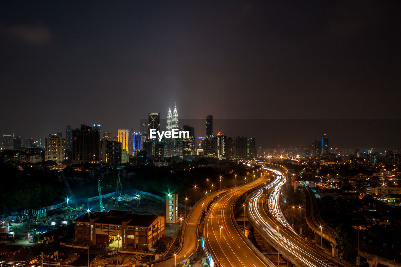 Illuminated modern buildings in city against sky at night