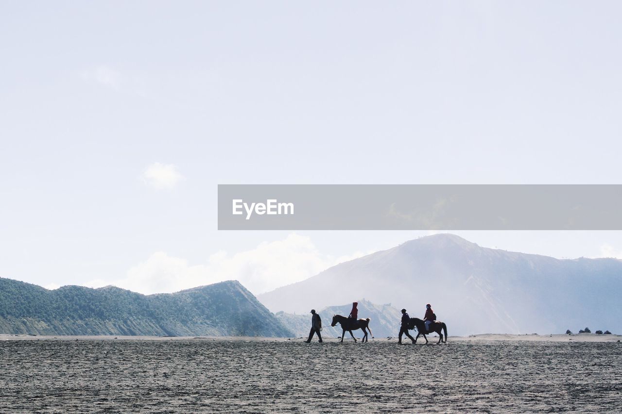 People riding horses on field against sky