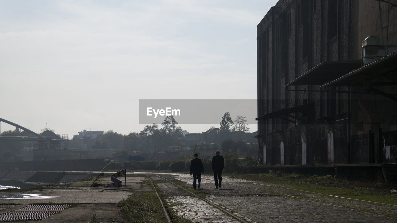 Two people walking on road along building