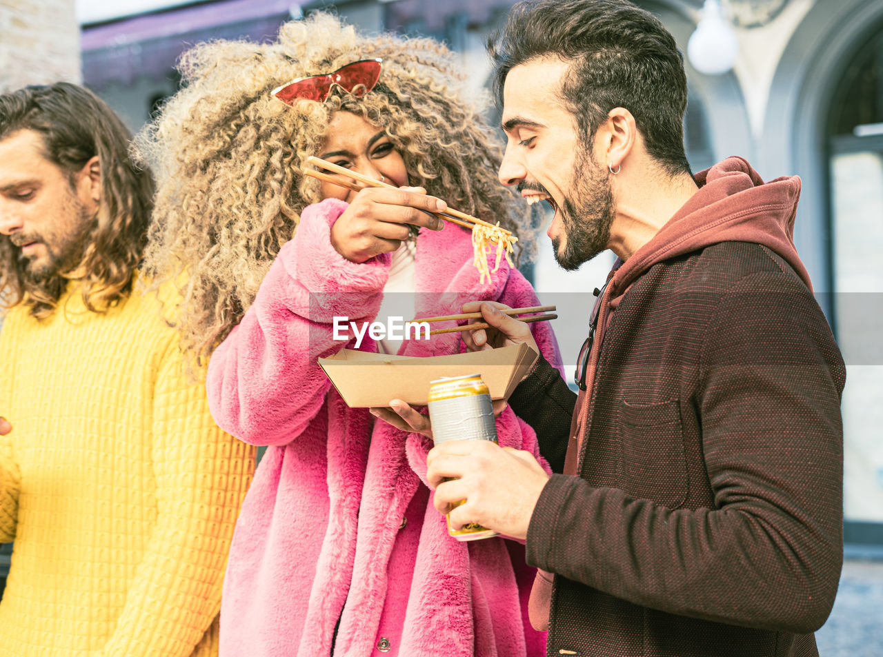 Woman feeding man holding drinking can by male