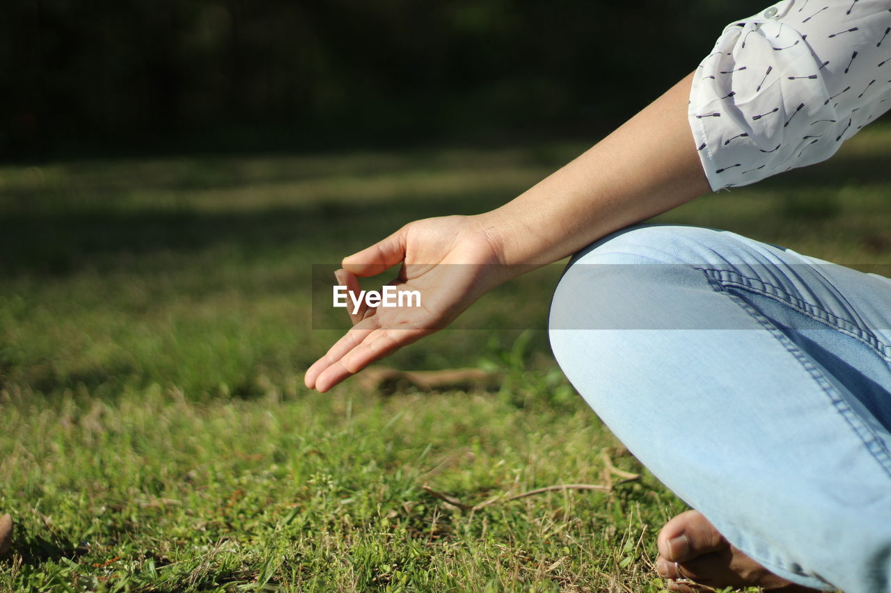 Midsection of woman doing yoga on field