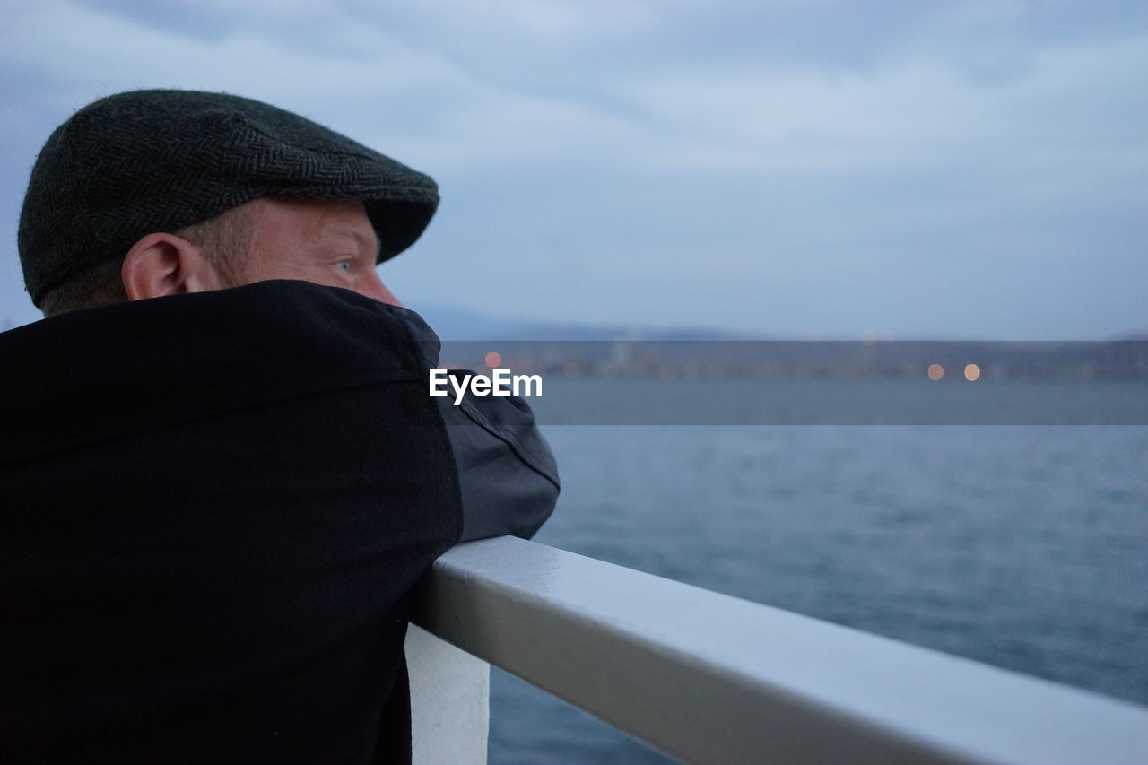 Close-up of man at railing by sea against sky