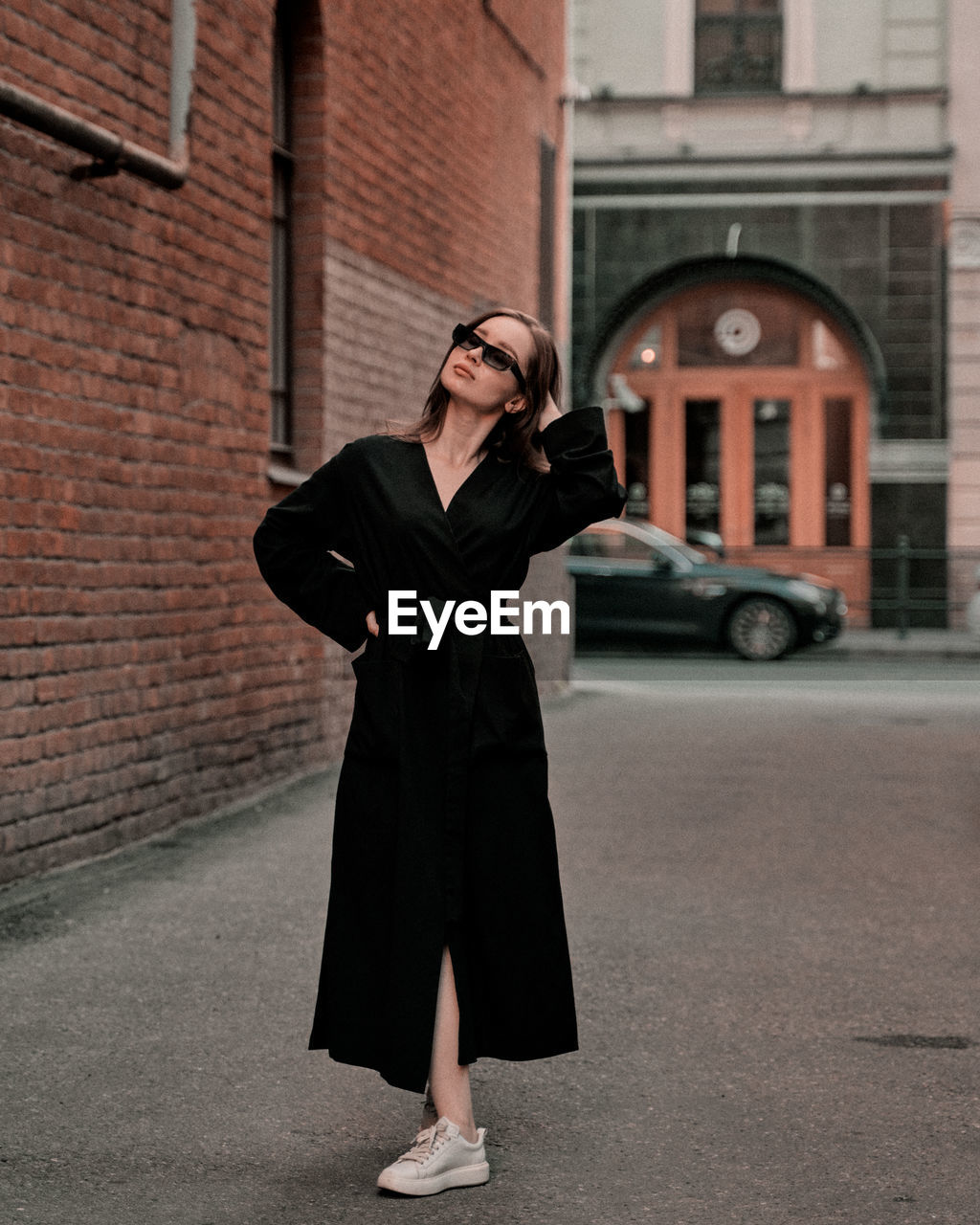 one person, adult, architecture, city, full length, black, standing, street, outerwear, clothing, coat, building exterior, women, young adult, fashion, road, built structure, dress, city life, front view, glasses, car, looking, portrait, communication, technology, transportation, spring, trench coat, female, lifestyles, day, outdoors