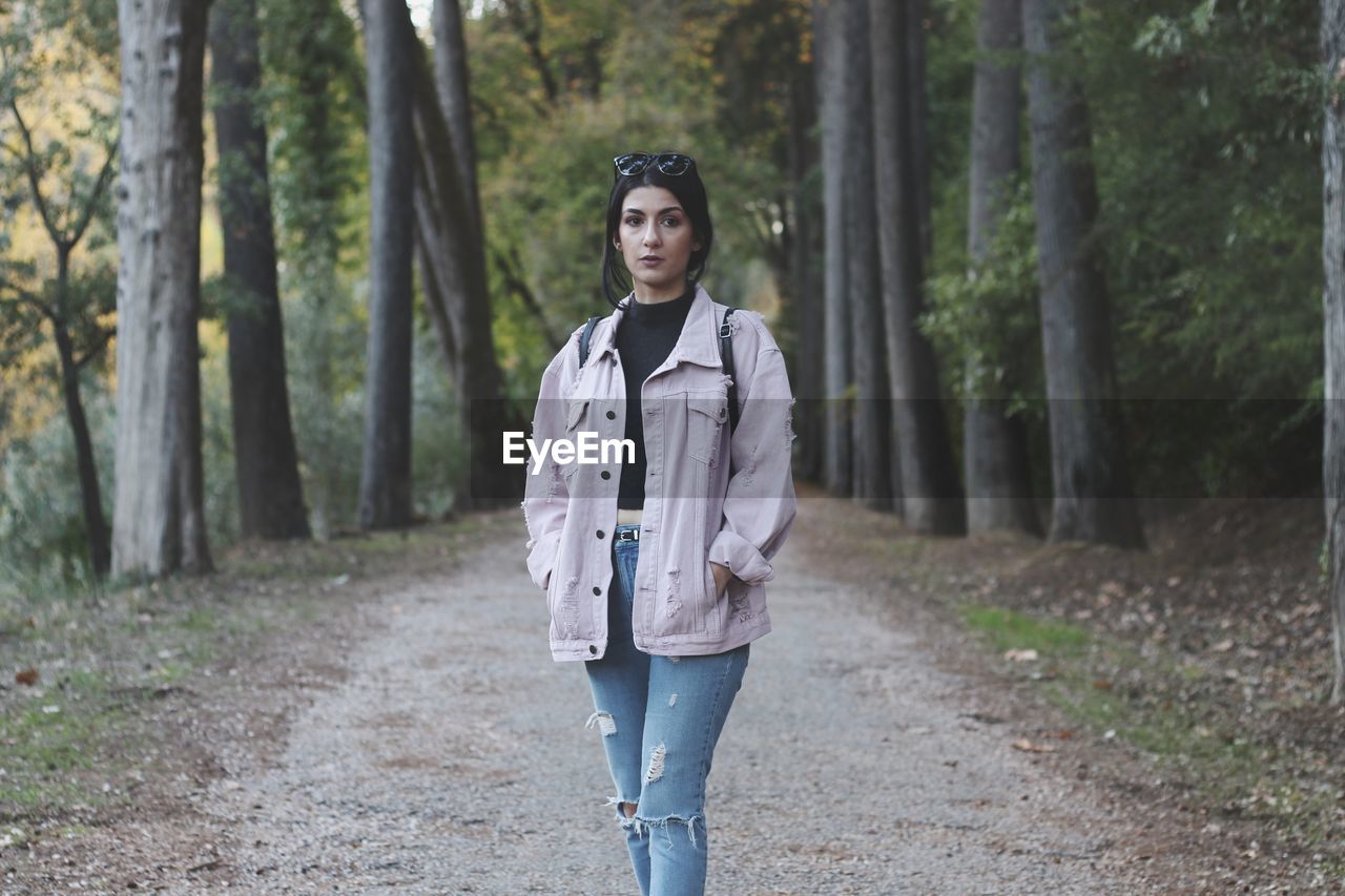 Portrait of young woman standing on road at forest