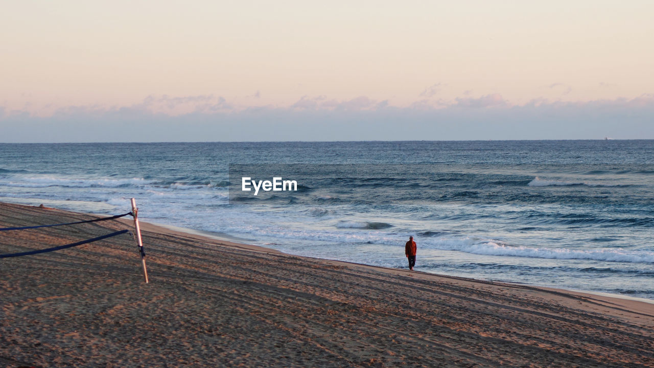 Rear view of man standing on beach against sky during sunset