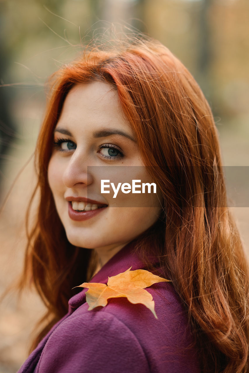 Autumn portrait of candid beautiful red-haired girl with fall leaves in hair.