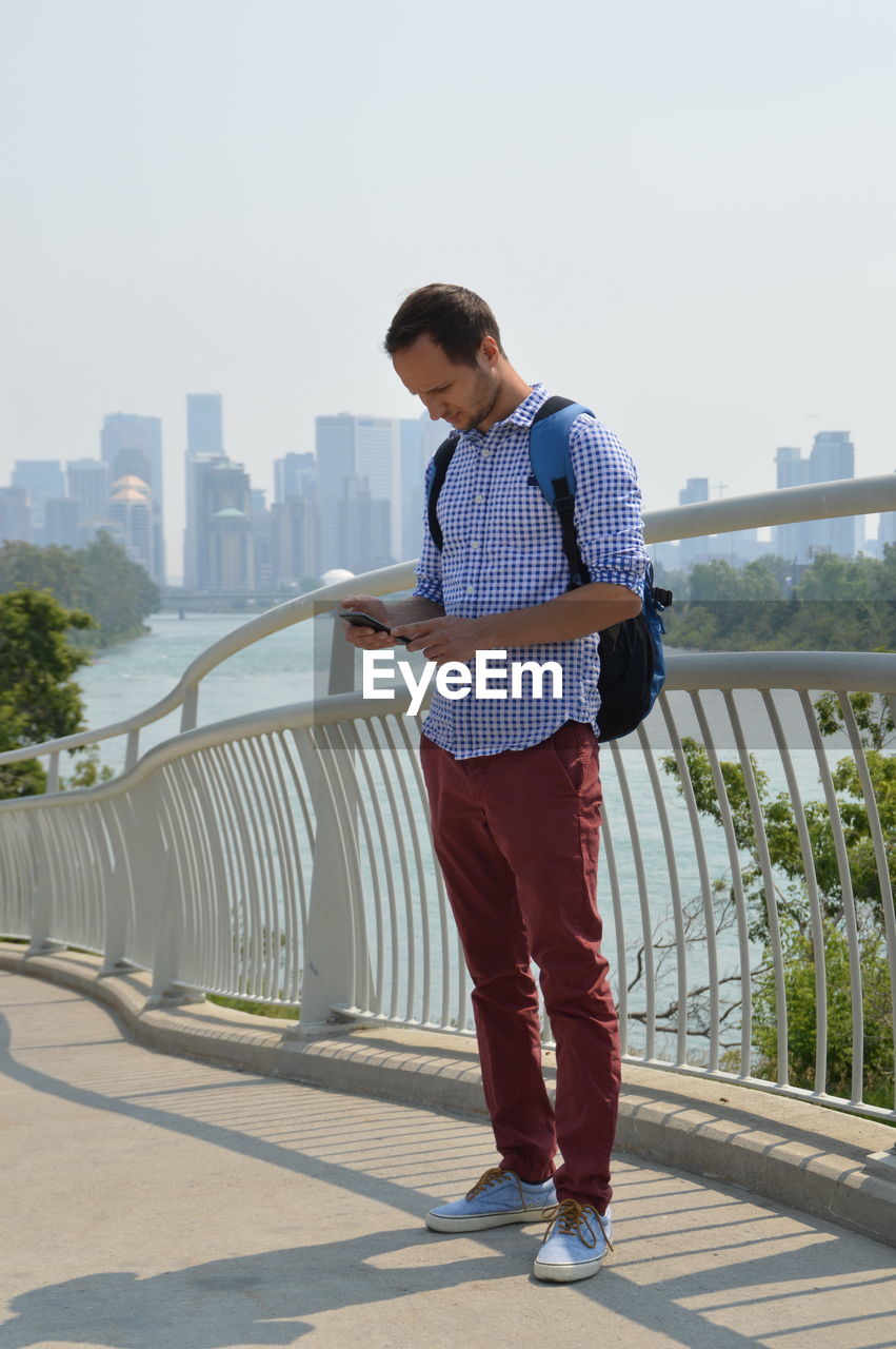 Man using mobile phone while standing on bridge against railing