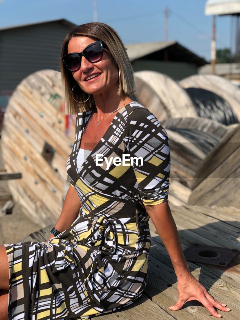 Portrait of smiling mature woman wearing sunglasses while sitting wooden spool